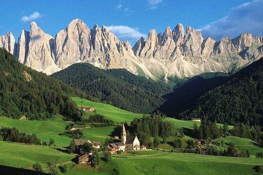 A mountainous landscape with a church, green fields, and rocky peaks. 1