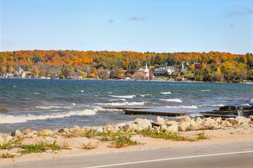 A lake with a rocky shoreline, a dock, and a forested hill with autumn-colored trees in the background. 2