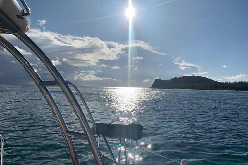 A boat's bow with a metal railing, calm water, and a sunlit landscape with a distant hill. 2