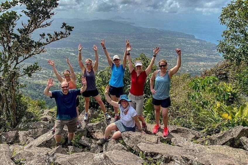 A group of people on a rocky outcrop with a scenic view of a valley and mountains in the background. 1