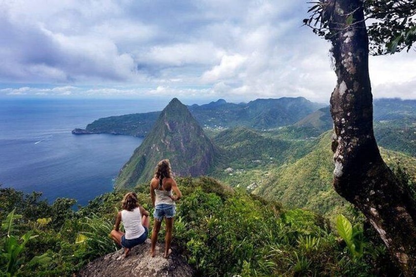 Two people standing on a hill overlooking a mountainous landscape with a view of the ocean. 4