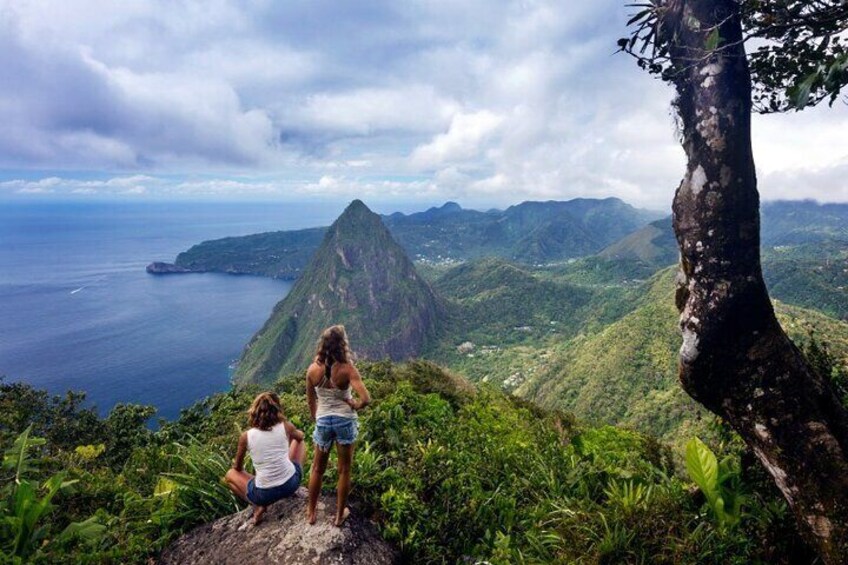 Two people standing on a mountain overlooking a coastal landscape with a prominent mountain peak. 5
