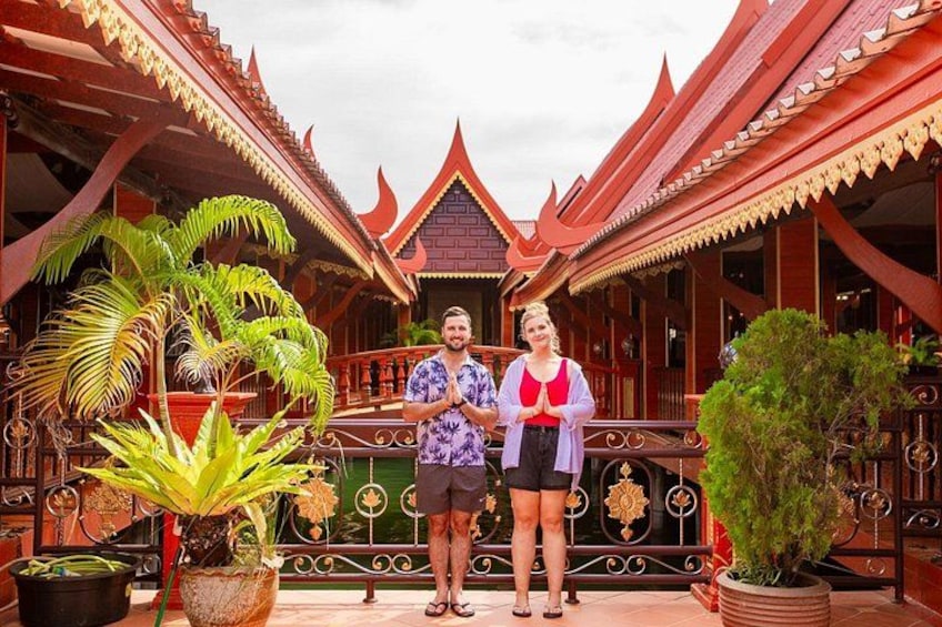 A traditional Thai building with ornate architecture, a couple standing in front, and potted plants. 3
