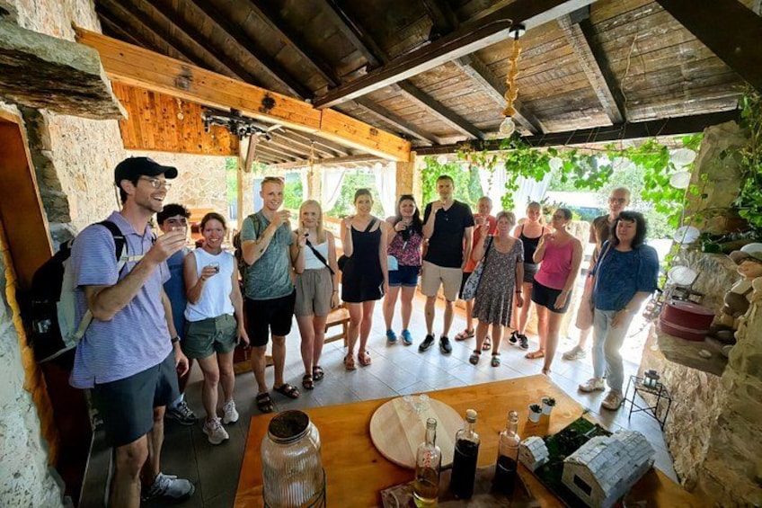Un groupe de personnes se tient dans un abri rustique en bois, doté de murs en pierre, avec une table en bois sur laquelle se trouvent des bouteilles et un verre, ainsi qu'une petite maquette de maison. 4