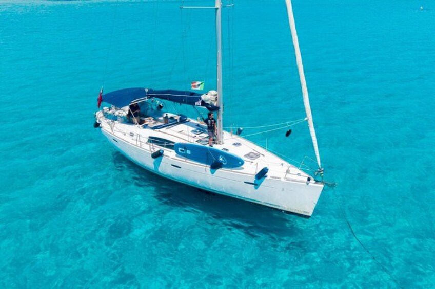 A sailboat with a blue canopy and a flag, floating on clear turquoise water. 4