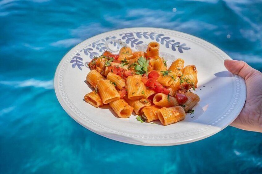 A plate of pasta with tomatoes and herbs, held over a pool. 5