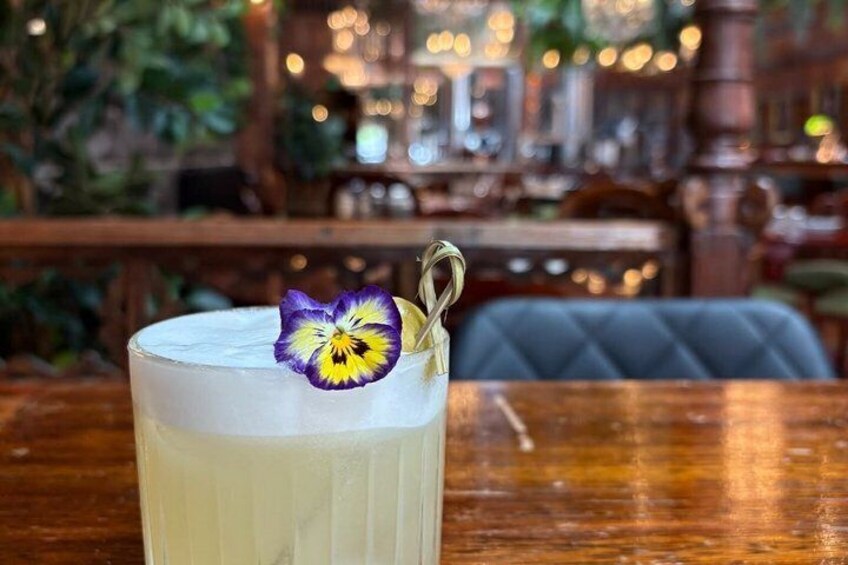 A glass of a creamy beverage with a purple flower garnish on a wooden table in a restaurant. 5