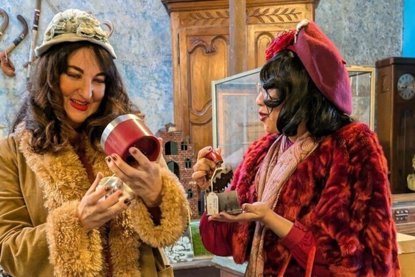 Two people in vintage clothing, one holding a red cup and the other holding a small box. 1
