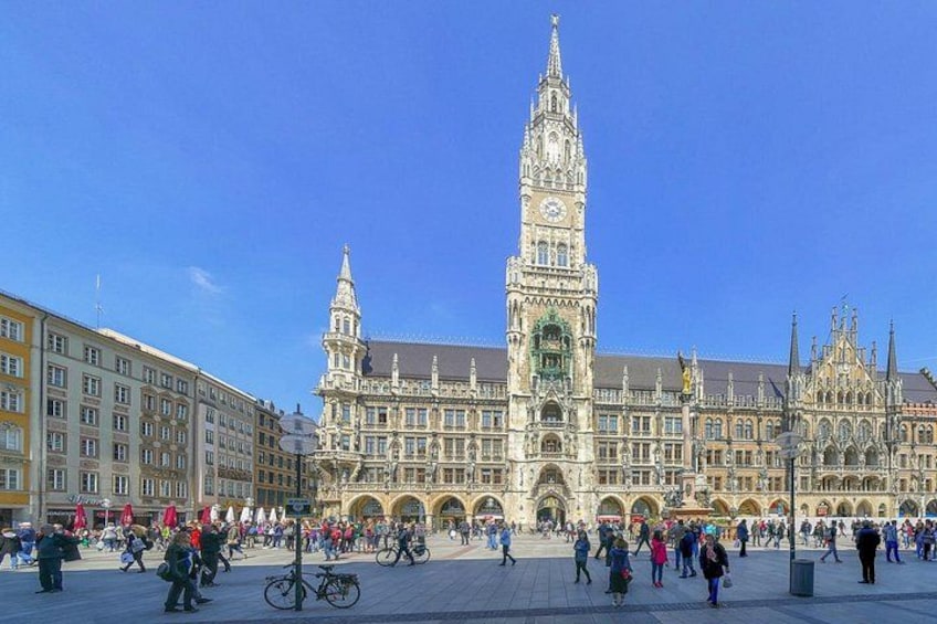A historic building with a clock tower, surrounded by a plaza with people and bicycles. 1