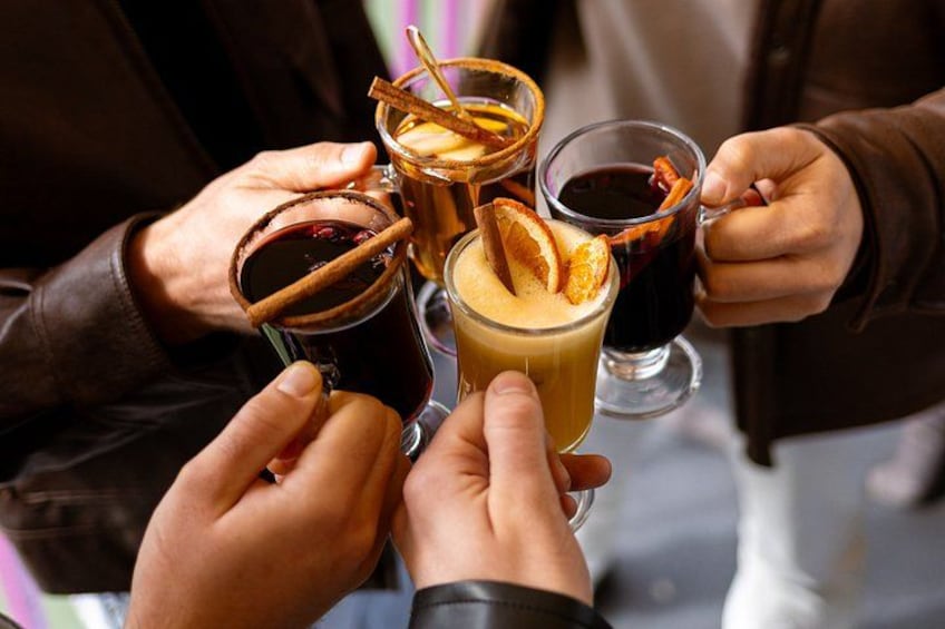 Four people holding glasses of beverages, some with cinnamon sticks and orange slices. 4
