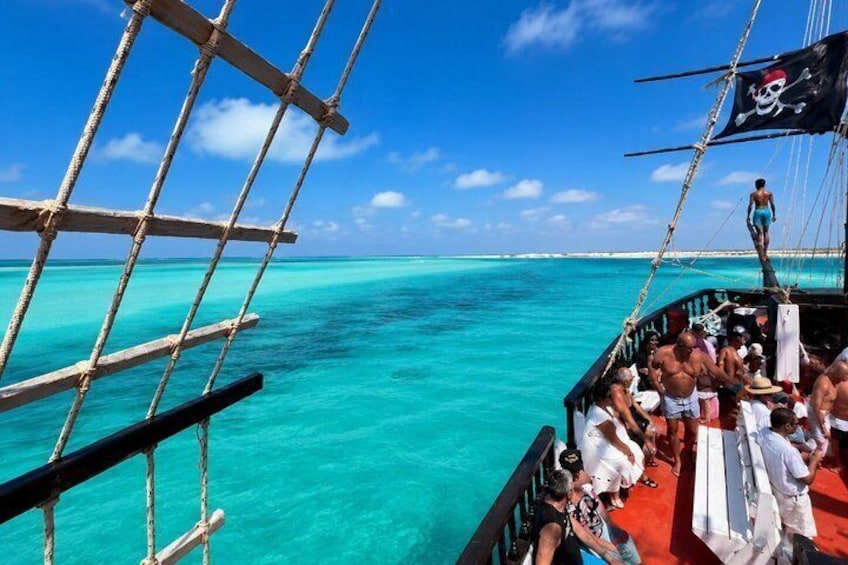 A sailboat with a pirate flag, passengers on deck, and turquoise ocean water. 1