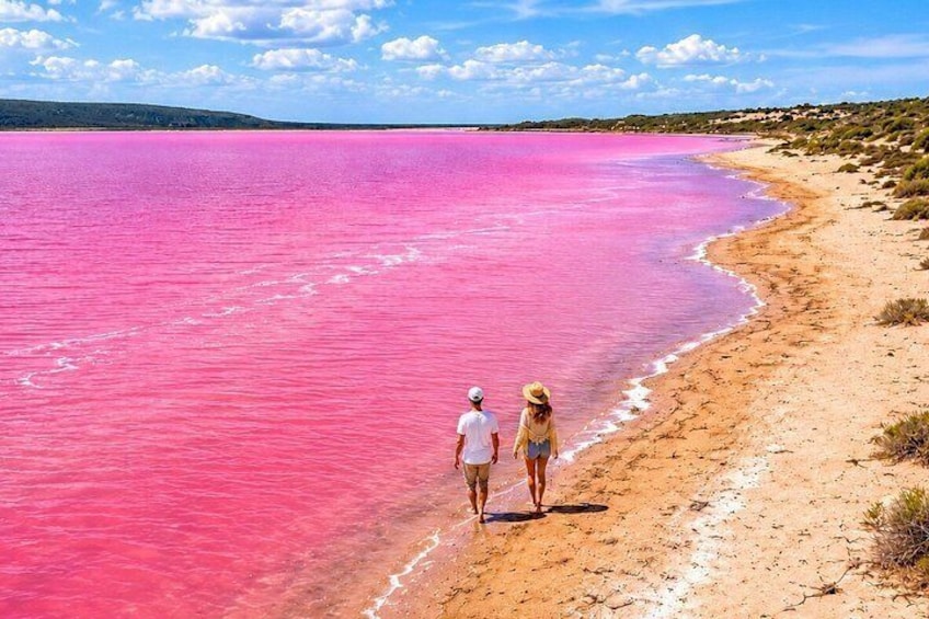 Un lago rosado, una playa arenosa y dos personas caminando por la orilla. 1
