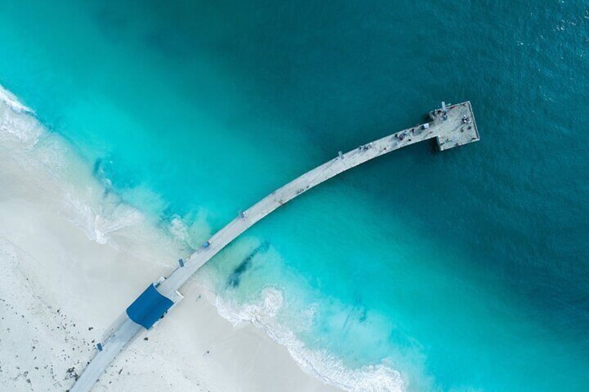 An aerial view of a white sandy beach with turquoise water and a long pier extending into the sea. 4