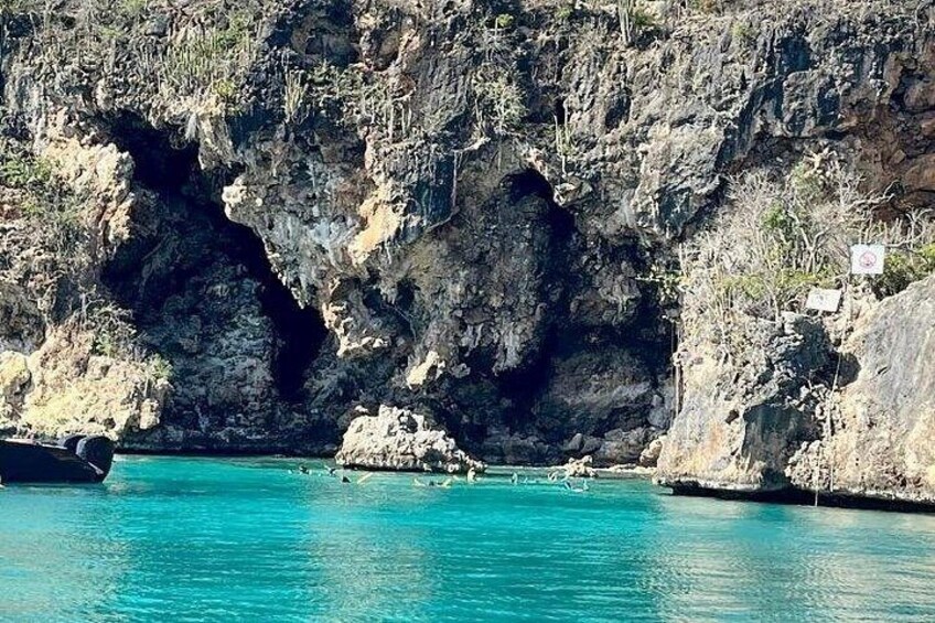 A coastal scene with a rocky cliff, clear turquoise water, and a boat. 1