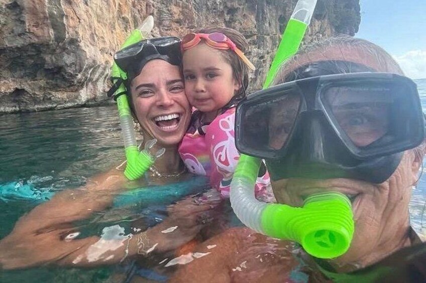 Two people snorkeling in a body of water with rocky cliffs in the background. 3