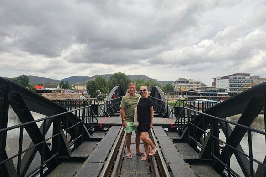 Two people standing on a bridge with a river and buildings in the background. 2