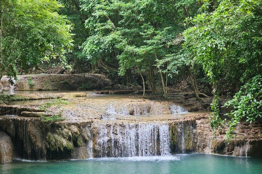 A waterfall cascading over rocky terrain into a clear pool surrounded by dense forest. 4