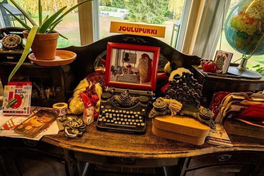 A desk with a typewriter, a globe, a framed picture, a plant, and various other items. 5