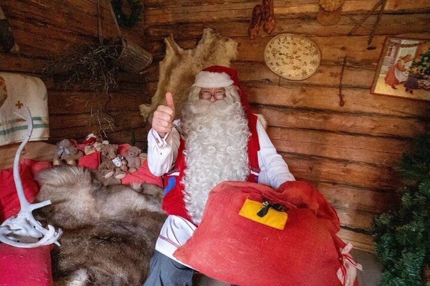 A person in a Santa Claus costume sitting in a rustic cabin with a red blanket and a yellow tag. 2