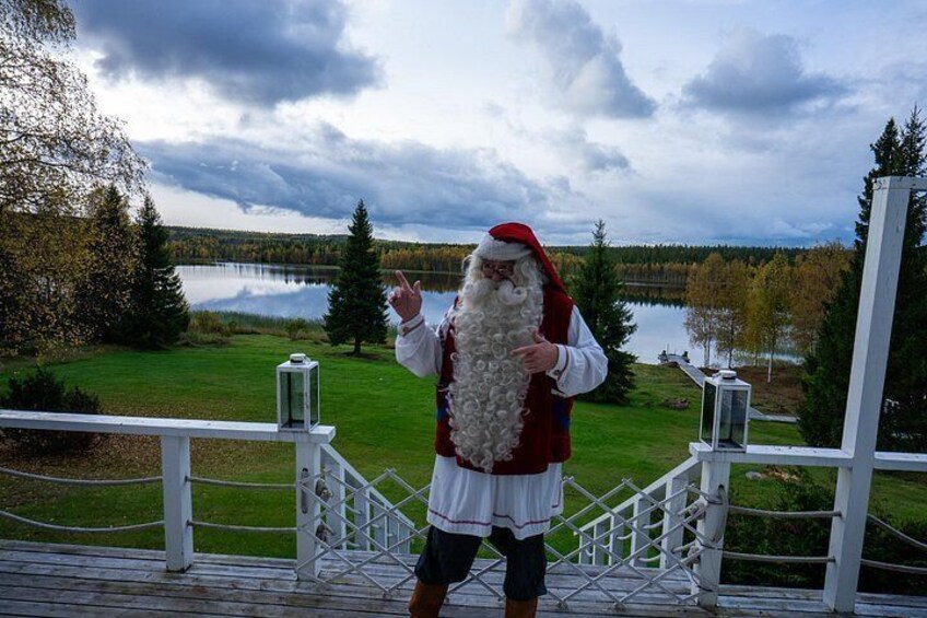 A person in a Santa costume standing on a wooden deck with a lake and trees in the background. 4