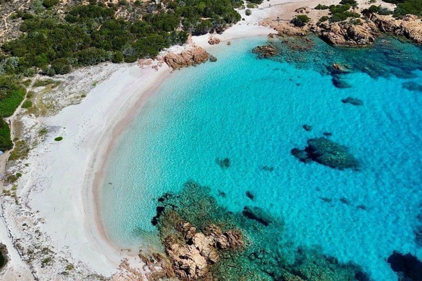 A coastal landscape with a sandy beach, clear turquoise waters, and rocky outcrops. 4