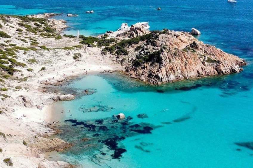 A coastal landscape with clear turquoise waters, rocky terrain, and a small island with a lighthouse. 3