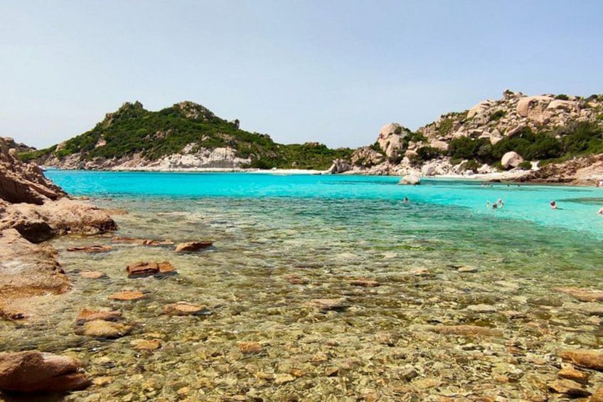 A clear turquoise sea, rocky shore, and green hills. 3