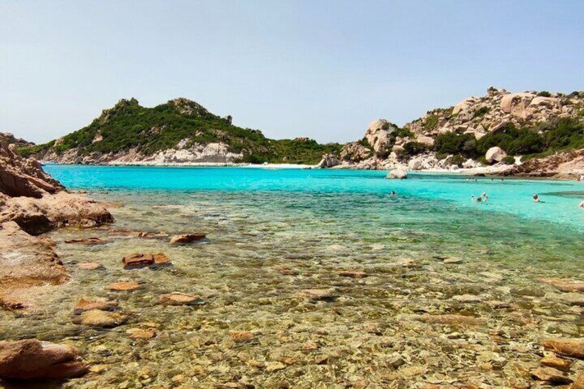 A clear turquoise sea with rocky shores and green hills in the background. 3