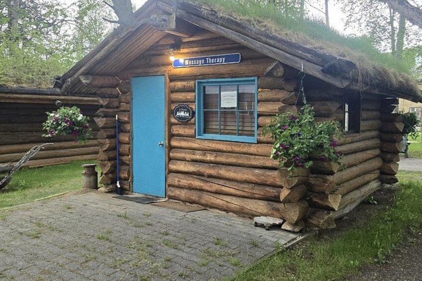 Une cabane en rondins avec une porte bleue et une enseigne indiquant « Massothérapie ». 3