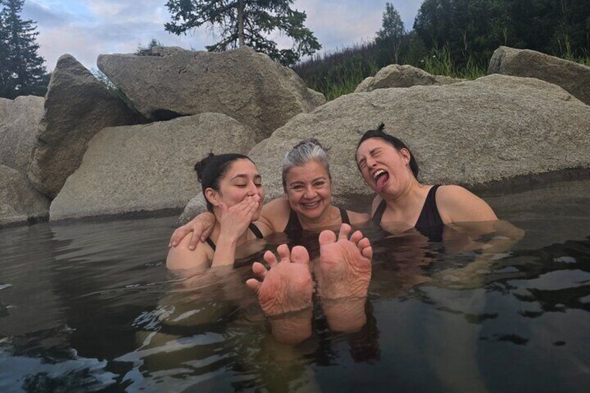 Three people in a natural hot spring surrounded by large rocks. 3