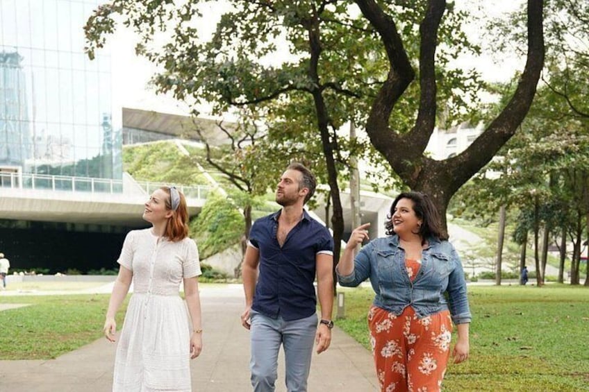 Three people walking on a path in a park with trees and a modern building in the background. 3