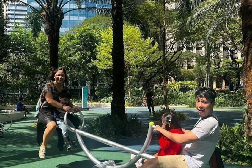 A park with exercise equipment, greenery, and a building in the background. 2