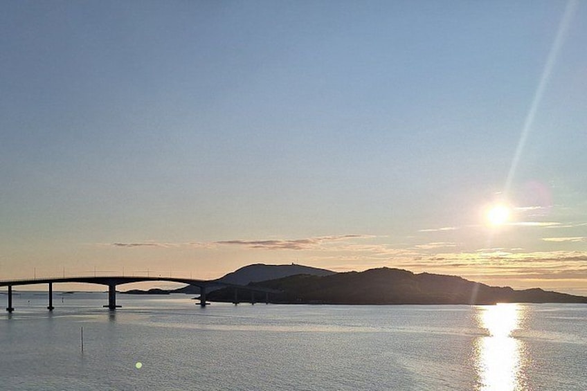 Un ponte sopra acque calme, con una montagna sullo sfondo e il sole che tramonta o sorge. 5
