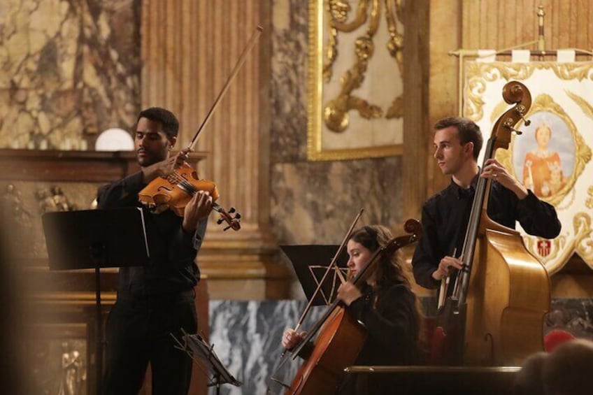 A string quartet performing in a grand hall with ornate decorations and a marble floor. 5