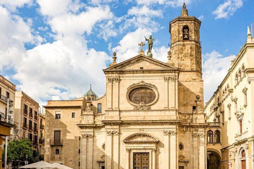 A historic church with a bell tower and statues, surrounded by old buildings. 2