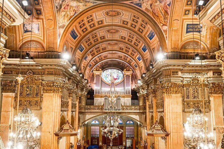 An ornate interior with a high ceiling, intricate carvings, and chandeliers. 4