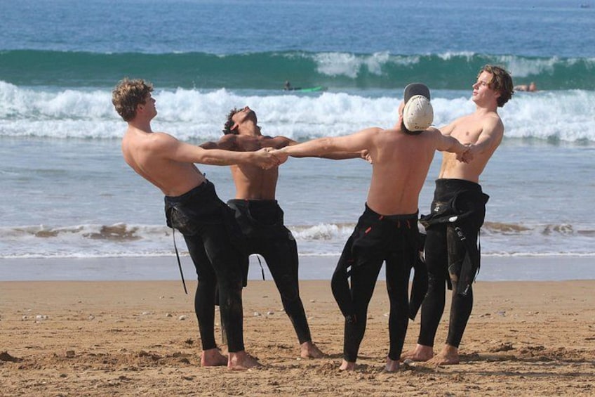 Four people on a beach, holding hands in a circle, with ocean waves in the background. 1