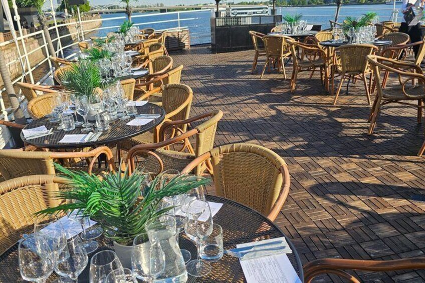 Een buitenterras met rieten stoelen en tafels, waarvan sommige versierd zijn met planten en lege wijnkaraffen. 5