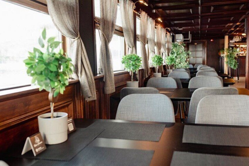 Een restaurantinterieur met houten lambrisering, grijze gestoffeerde stoelen en potplanten. 3
