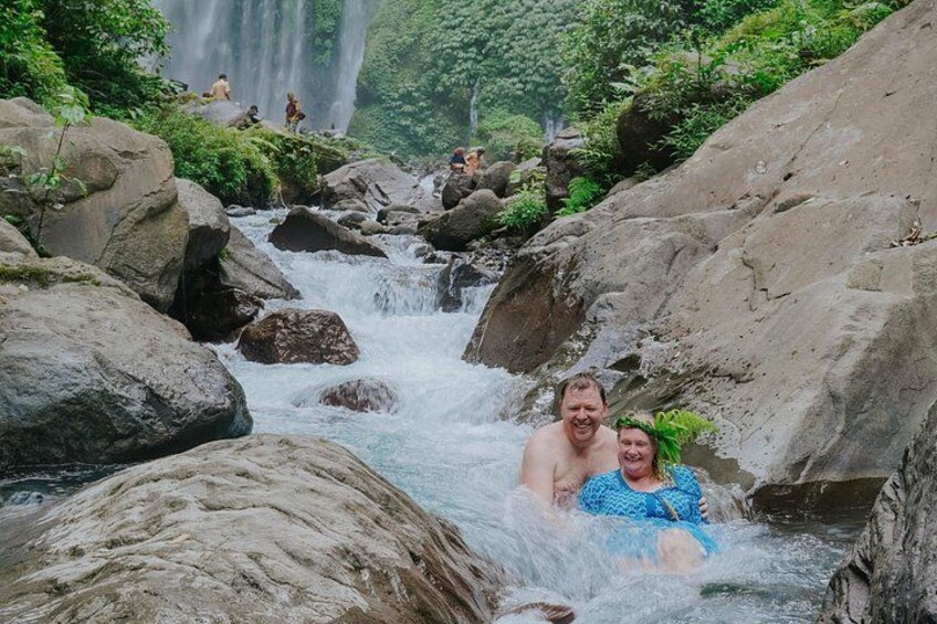 A river with rocks, a waterfall in the background, and people in the water. 2