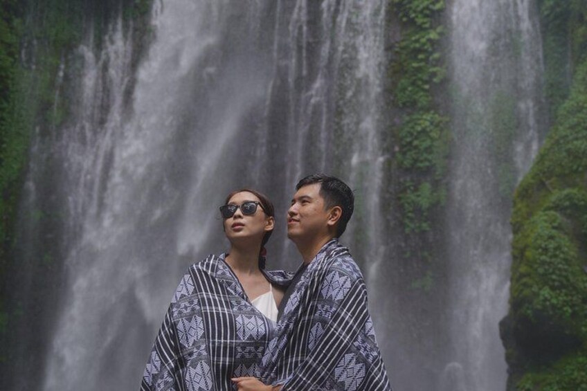 A waterfall with a couple standing in front of it. 4