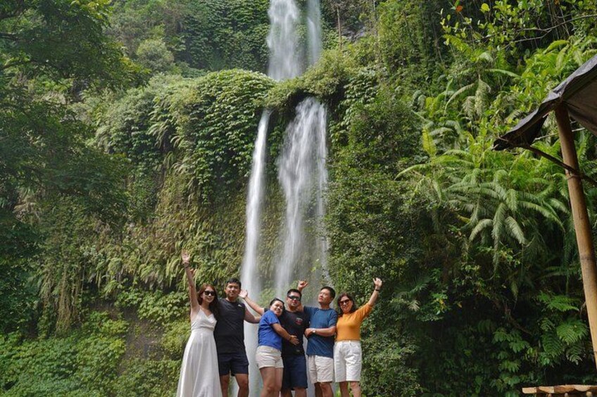 A group of people standing in front of a waterfall surrounded by lush greenery. 3