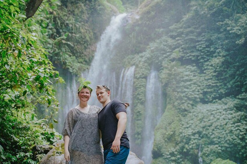 Two people standing in front of a waterfall with lush greenery in the background. 5