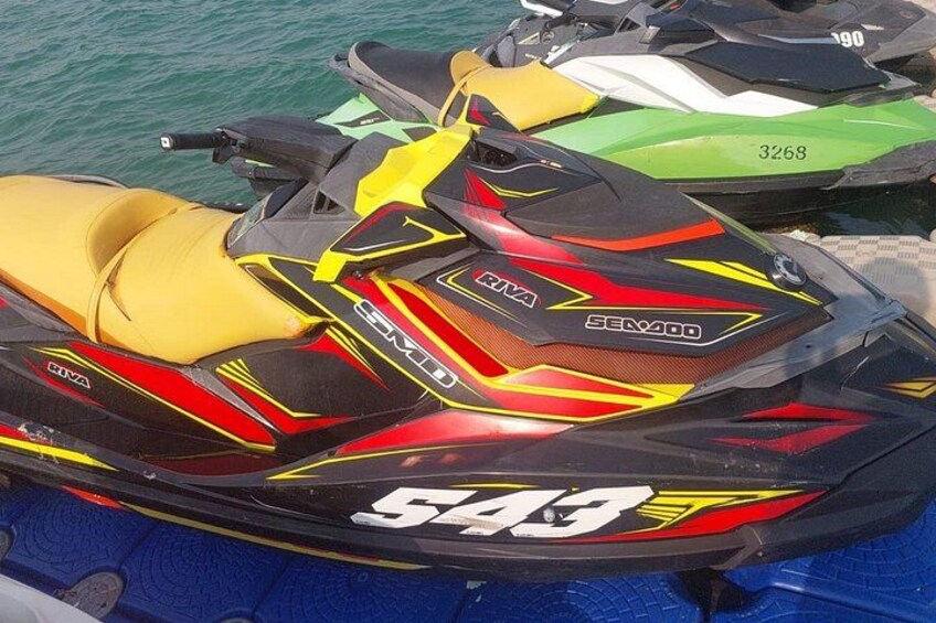 A yellow and black Sea-Doo 543 jet ski with a red and yellow design, docked near other watercraft. 1