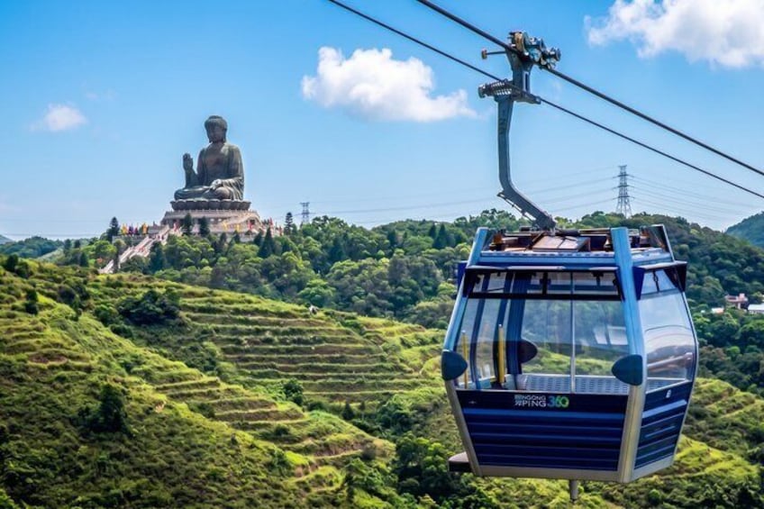 A cable car with 'Spring 360' written on it, a large Buddha statue, and terraced hills in the background. 1