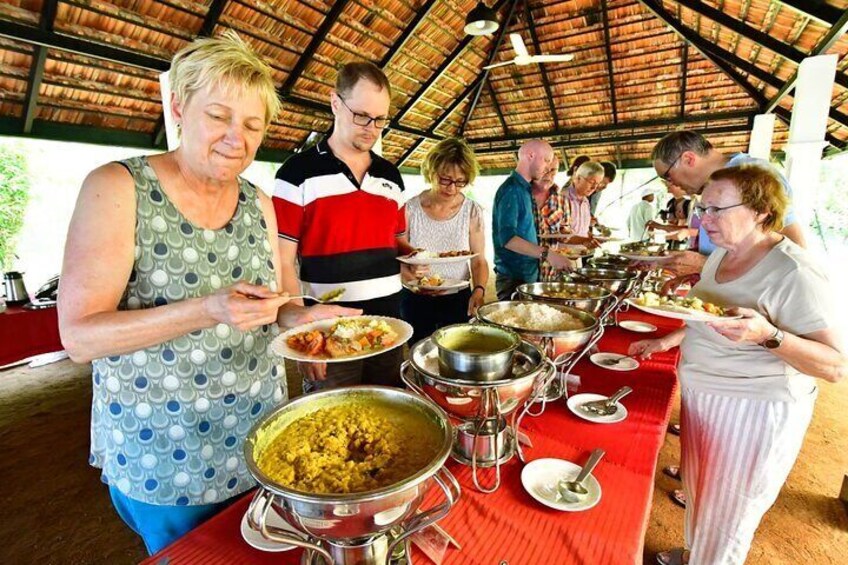 People dining at an outdoor event with various dishes on a long table. 3