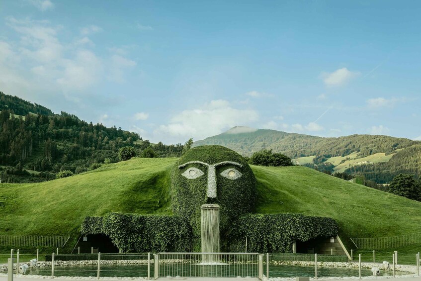 A landscape with a large, grassy hill shaped like a face, a small building, and a waterfall. 1