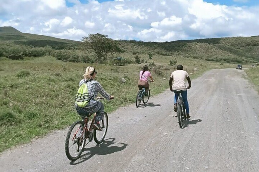 Three people riding bicycles on a dirt road surrounded by grassy hills. 1
