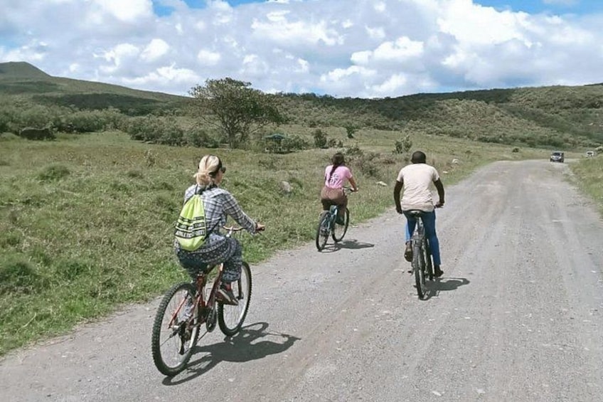 Three cyclists on a rural road with grassy fields and hills in the background. 1