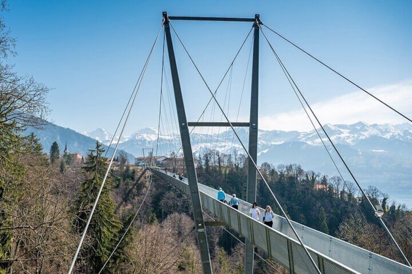 A suspension bridge with people walking on it, surrounded by mountains and trees. 1